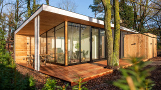 Modern glamping accommodation with large glass windows and wood paneling, set in a forest area.
