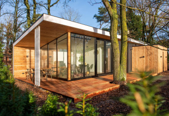 Hébergement glamping moderne avec de grandes baies vitrées et un bardage en bois, en pleine forêt.