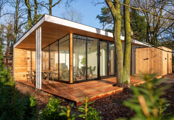 Alloggio glamping moderno con grandi vetrate e rivestimento in legno, immerso in una zona boschiva.