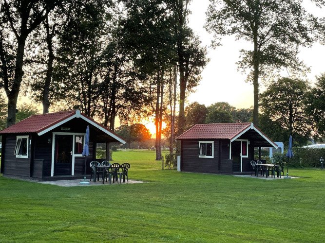 Dos acogedoras cabañas con terraza y muebles de jardín al atardecer en Recreation Park Den Blanken, Países Bajos.