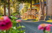 Vue ensoleillée du lodge Edelweiss, cabanes en bois, fleurs colorées et arbres majestueux alentour.