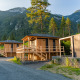 Træhytter ved Edelweiss-lodgen i bjergene, omgivet af grønne træer og malerisk natur under blå himmel.