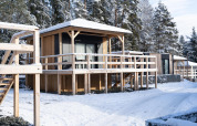 Cabañas de madera en Edelweiss lodge nevado, con ventanas de cristal, terrazas elevadas y bosque atrás.