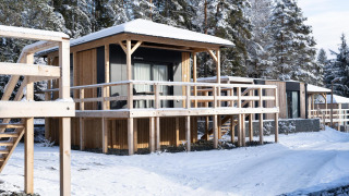 Chalets en bois du lodge Edelweiss sous la neige, fenêtres vitrées, terrasse surélevée et forêt derrière.
