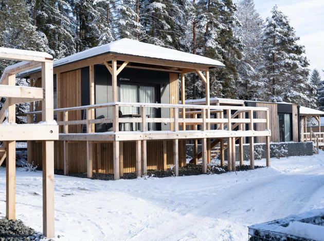 Houten lodges bij de besneeuwde Edelweiss lodge met glazen ramen, terras en bos op de achtergrond.