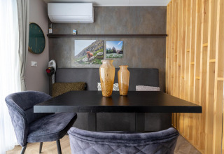 Moderne eethoek in de Edelweiss-lodge met zwarte stoelen, vazen, wandklok en houten lambrisering.