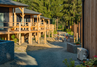 Famiglia in bicicletta davanti ai bungalow in legno dell’Edelweiss Lodge, immersi nel verde degli alberi.