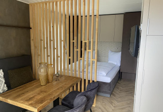 Habitación de lodge moderna en Edelweiss con separador de madera, cama cómoda, mesa y sillas elegantes.