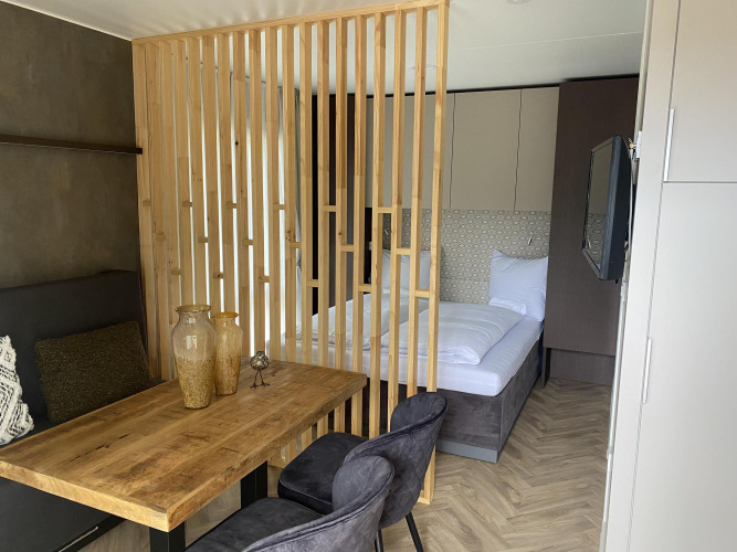 Moderne lodgekamer bij Edelweiss met houten afscheiding, comfortabel bed, eettafel en stoelen in licht interieur.