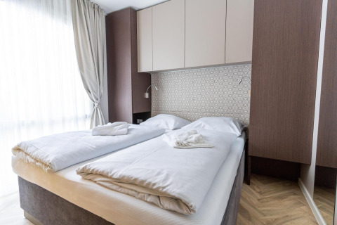 Modernes Zimmer in der Lodge Edelweiss mit zwei Betten, weißen Decken und elegantem, hellem Design.
