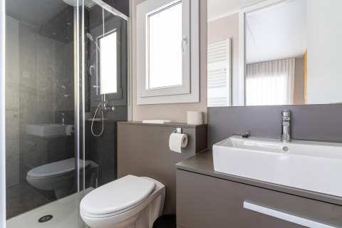 Modern badkamer in Edelweiss-lodge met glazen douche, toilet, wastafel en groot raam met licht.