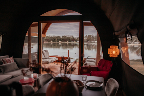 Interno accogliente di una Waterlodge con vista lago attraverso grandi finestre a De Achterste Hoef, Paesi Bassi.