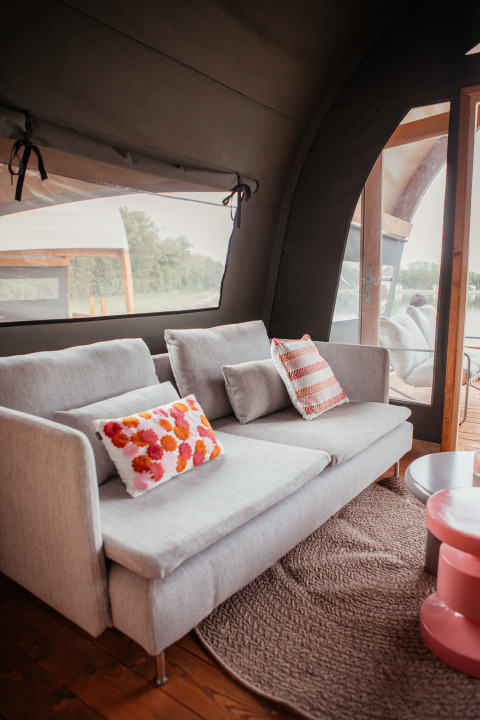 Moderne woonkamer in een Waterlodge op Recreatiepark De Achterste Hoef, met zetel en kleurrijke kussens.
