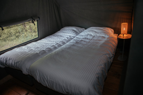 Due letti singoli in una Waterlodge al Recreatiepark De Achterste Hoef, Paesi Bassi, con lampada accesa.