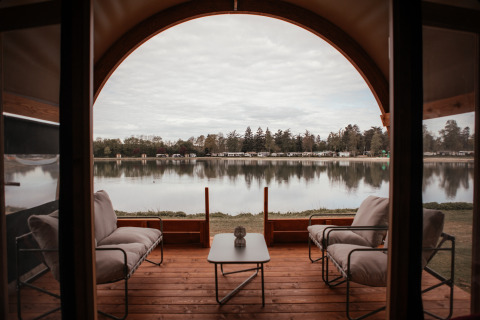 Vista lago dalla terrazza della Waterlodge al Recreatiepark De Achterste Hoef, Paesi Bassi, con sedie comode.