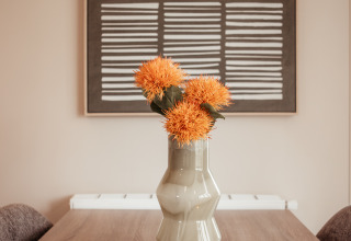 Mesa de madera moderna con florero, flores naranjas y arte mural en Luxury Chalet, De Achterste Hoef, Países Bajos.