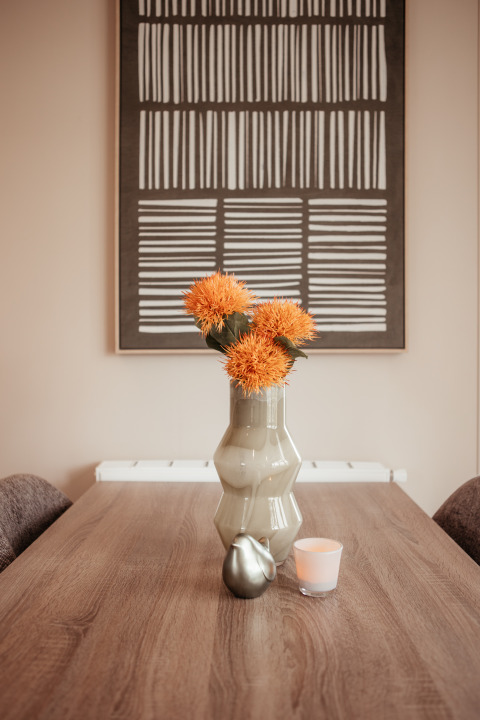 Mesa de madera moderna con florero, flores naranjas y arte mural en Luxury Chalet, De Achterste Hoef, Países Bajos.