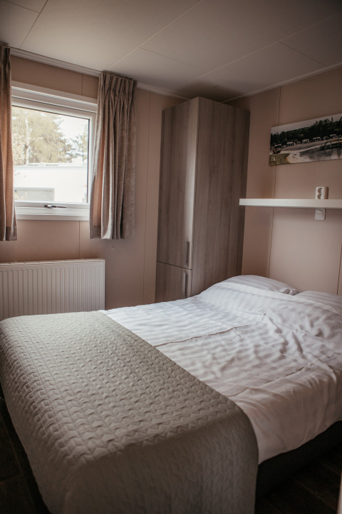 Dormitorio con cama doble, armario y ventana en un chalet de lujo en Recreatiepark De Achterste Hoef, Países Bajos.
