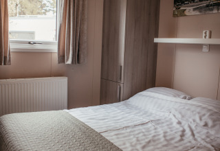 Dormitorio con cama doble, armario y ventana en un chalet de lujo en Recreatiepark De Achterste Hoef, Países Bajos.