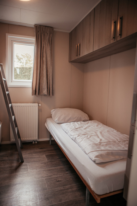 Knusse eenpersoonskamer met bed, raam, ladder en kasten in een luxueus chalet in Nederland.