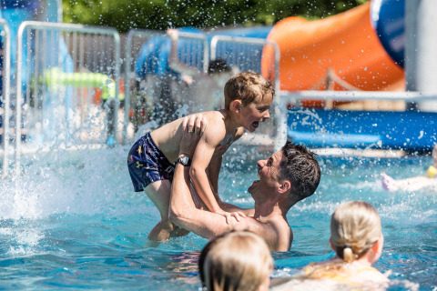 Far og søn leger sammen i poolen på Kampeerdorp de Zandstuve, en feriepark i Overijssel, Holland.