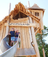 Dos niños juegan en un gran parque infantil de madera con tobogán en Kampeerdorp de Zandstuve, Overijssel.