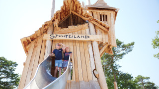Zwei Kinder spielen auf einem großen Holzspielplatz mit Rutsche im Kampeerdorp de Zandstuve, Overijssel.