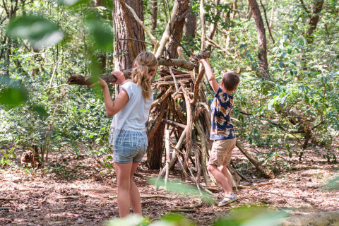 Dos niños construyen una cabaña con ramas en el bosque en Kampeerdorp de Zandstuve, Overijssel, Países Bajos.