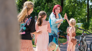 Kinder spielen und lachen mit einer verkleideten Darstellerin im Kampeerdorp de Zandstuve, Overijssel, Niederlande.