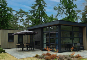 Lodge L-Cube 4+2 moderne à De Utrechtse Heuvelrug, Pays-Bas, entouré d’arbres et terrasse extérieure paisible.