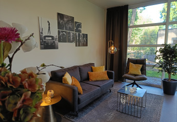 Moderne zithoek in L-Cube 4+2 lodge aan De Utrechtse Heuvelrug, Nederland, met grote ramen en sfeervol design.