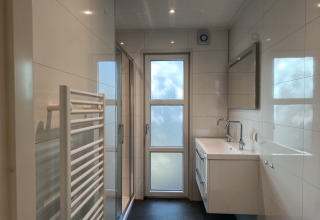 Salle de bain moderne et lumineuse dans le lodge L-Cube 4+2 à De Utrechtse Heuvelrug, Pays-Bas, avec douche vitrée.