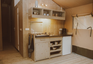 Angolo cucina di tenda safari di lusso con legno, fornello a gas, lavello, mini frigo e scaffali nei Paesi Bassi.