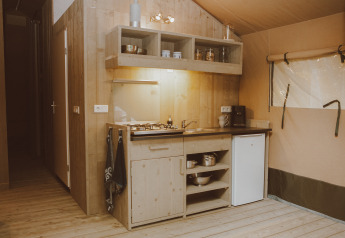 Coin cuisine d’une tente safari de luxe avec bois, gazinière, évier et mini-réfrigérateur aux Pays-Bas.