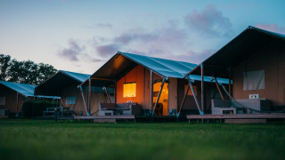 Safari-Zelte im Holiday park De Boshoek in den Niederlanden bei Dämmerung, warm beleuchtet, grüne Wiese.
