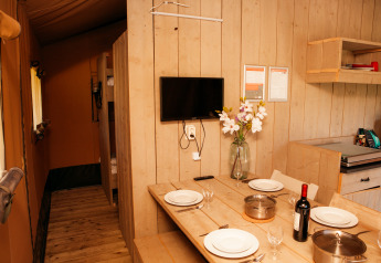 Indvendig udsigt af Safari telt ved Holiday park De Boshoek, med spisebord, køkken og tv på væggen.