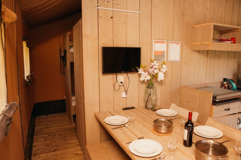Innenansicht des Safari-Zelts im Holiday Park De Boshoek, mit Esstisch, Küche und Fernseher an der Wand.