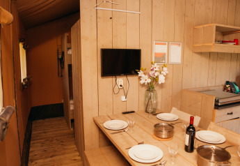 Vista interior de la Safari Tent en Holiday park De Boshoek, con mesa de comedor, cocina y TV en la pared.