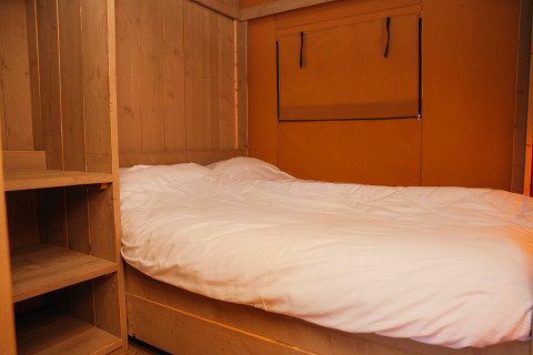 Schlafbereich im Safari-Zelt im Ferienpark De Boshoek, Niederlande, mit Holzregalen und Bett.