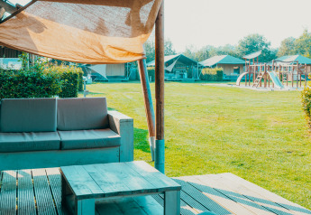 Blick von der Terrasse eines Safari-Zeltes im Ferienpark De Boshoek mit Spielplatz und Rasen.
