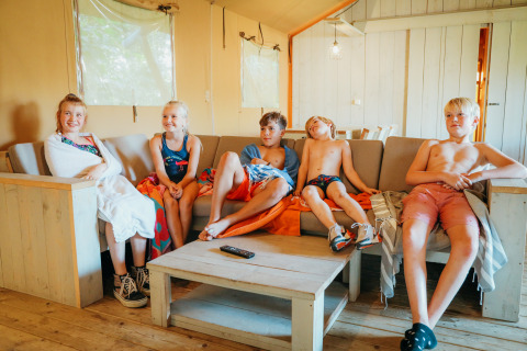 Børn sidder afslappet på en sofa inde i en safari-teltvilla ved ferieparken De Boshoek i Holland.