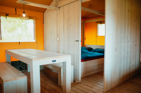 Interiør af Safari Villa teltet i De Boshoek, Holland, med træbord, bænke og soveområde.