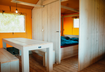 Intérieur de la tente Safari Villa au parc De Boshoek, Pays-Bas, avec table et lit en bois.