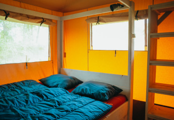 Vista interna della tenda Safari Villa con letto matrimoniale e scala di legno a De Boshoek, Paesi Bassi.