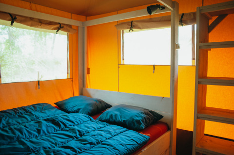 Vista interior de la tienda Safari Villa con cama doble y escalera de madera en De Boshoek, Países Bajos.