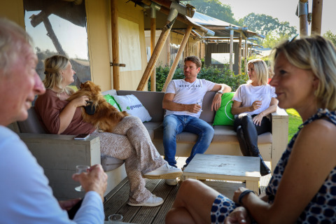 Fünf Erwachsene entspannen sich und unterhalten sich auf der Terrasse eines Safari-Zeltes bei De Boshoek, Niederlande.