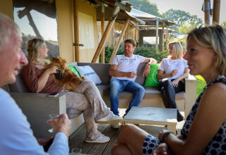 Cinco adultos conversan y se relajan en la terraza de una tienda Safari Villa en el parque De Boshoek, Países Bajos.