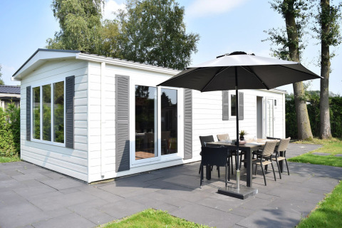 Veluwelodge met witte buitenkant, terras, parasol en tuinmeubilair op Holiday park De Boshoek in Nederland.