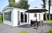 Veluwelodge con fachada blanca, terraza, sombrilla y muebles de exterior en Holiday park De Boshoek, Países Bajos.