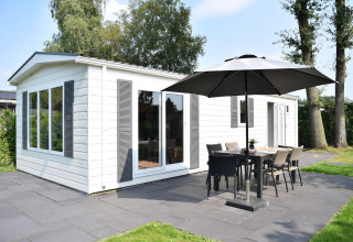 Veluwelodge con fachada blanca, terraza, sombrilla y muebles de exterior en Holiday park De Boshoek, Países Bajos.